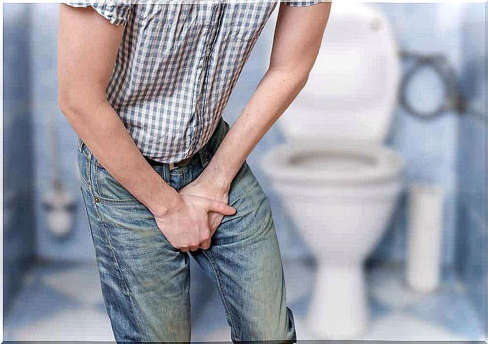 A man standing in the bathroom holding his groin.