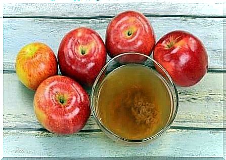 Apples lying around a glass of apple cider vinegar