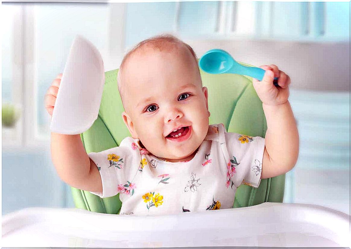 A baby holding the bowl and spoon in the air.